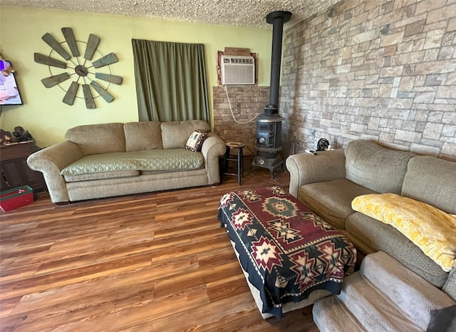 living room with hardwood / wood-style floors, an AC wall unit, a textured ceiling, and a wood stove