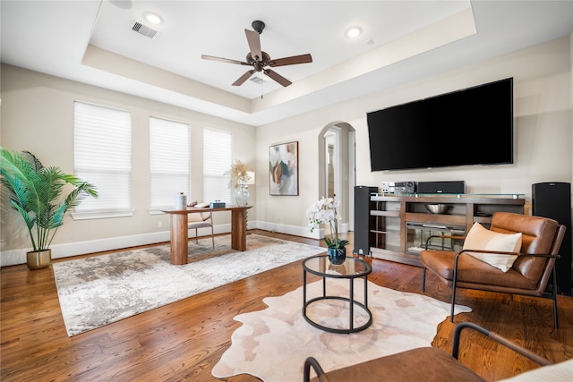 living room with hardwood / wood-style flooring, ceiling fan, and a raised ceiling