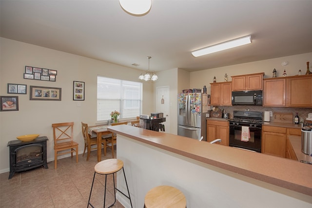 kitchen with black appliances, kitchen peninsula, an inviting chandelier, backsplash, and hanging light fixtures