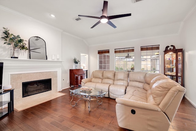 living room featuring ceiling fan, dark wood-type flooring, lofted ceiling, a tiled fireplace, and ornamental molding