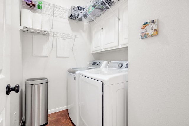 clothes washing area featuring cabinets, washing machine and dryer, and dark tile patterned flooring