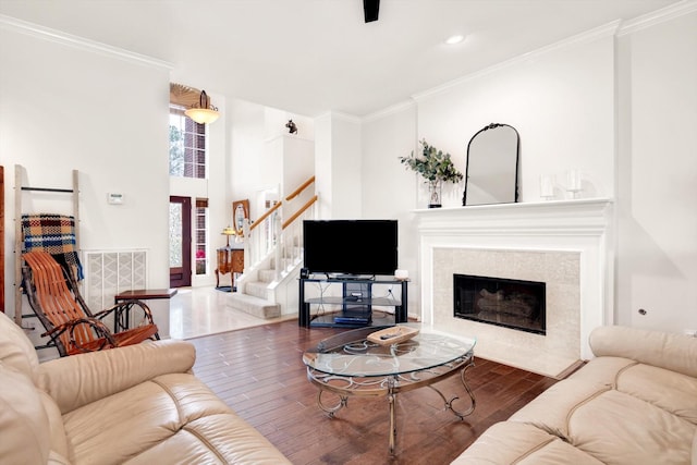 living area featuring visible vents, ornamental molding, a tiled fireplace, wood finished floors, and stairway