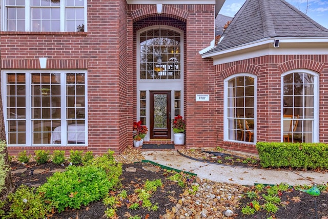 doorway to property with brick siding and a shingled roof