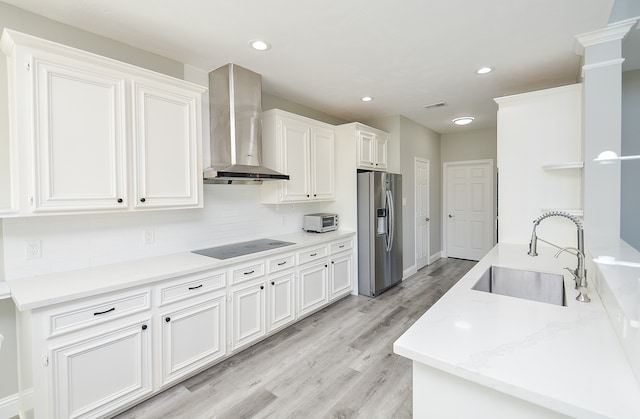 kitchen featuring black electric stovetop, wall chimney exhaust hood, sink, white cabinetry, and stainless steel fridge