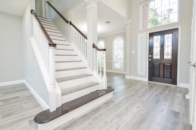 foyer entrance with light wood-type flooring, plenty of natural light, crown molding, and decorative columns