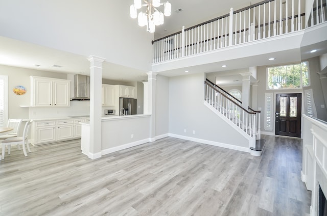 unfurnished living room with a towering ceiling, light wood-type flooring, decorative columns, and an inviting chandelier