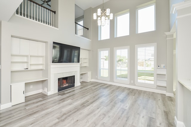 unfurnished living room featuring a premium fireplace, a towering ceiling, an inviting chandelier, and light hardwood / wood-style floors