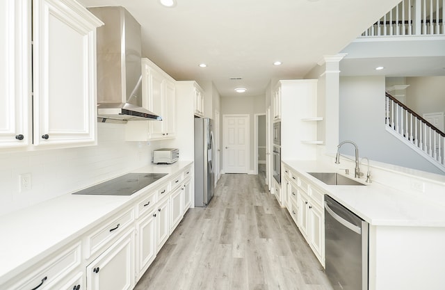 kitchen with stainless steel appliances, white cabinetry, wall chimney range hood, sink, and light hardwood / wood-style floors