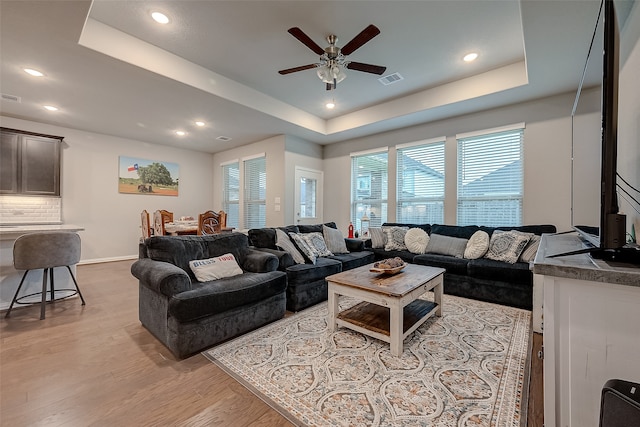 living room featuring a tray ceiling, ceiling fan, and light wood-type flooring