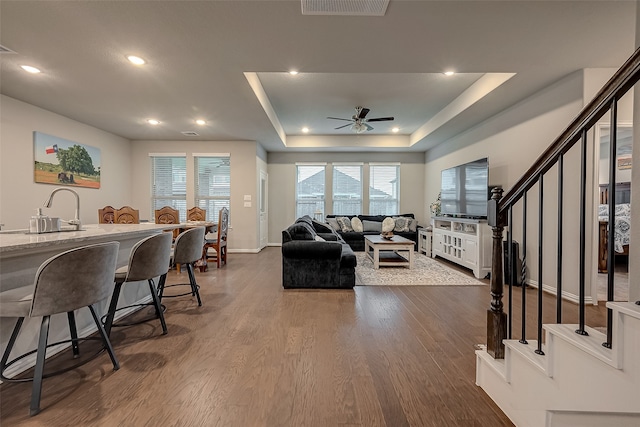 living room with dark hardwood / wood-style flooring, a raised ceiling, ceiling fan, and sink