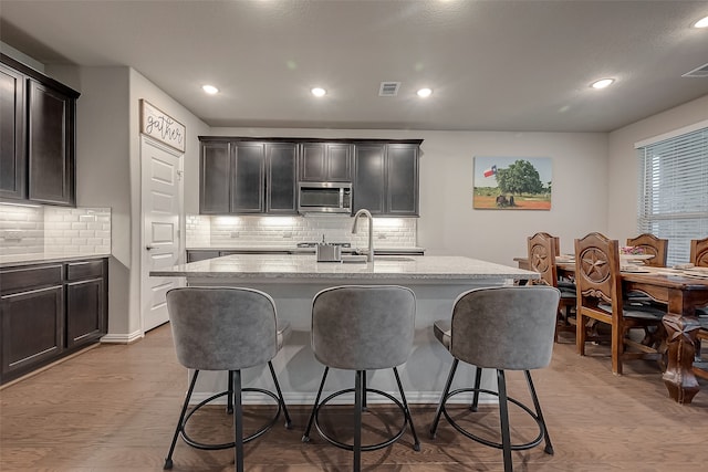 kitchen featuring light stone counters, light wood-type flooring, and an island with sink