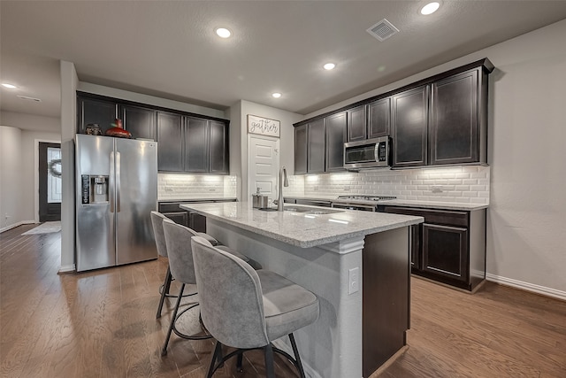 kitchen featuring decorative backsplash, appliances with stainless steel finishes, a kitchen breakfast bar, a kitchen island with sink, and wood-type flooring