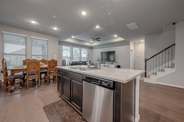 kitchen with dishwasher, a center island with sink, sink, light wood-type flooring, and a tray ceiling