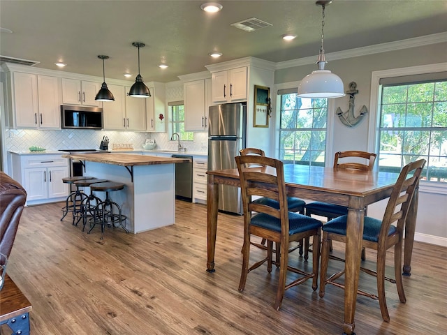 kitchen with white cabinets, decorative light fixtures, stainless steel appliances, and ornamental molding