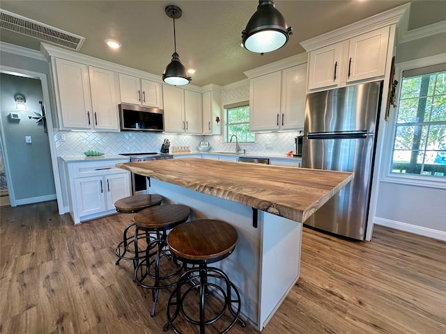 kitchen featuring white cabinetry, ornamental molding, decorative light fixtures, and appliances with stainless steel finishes