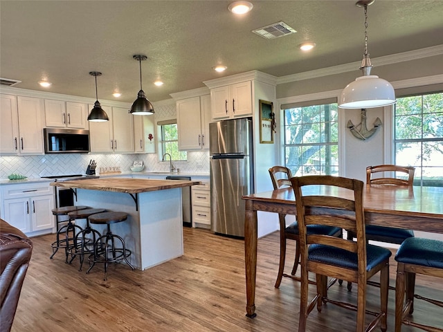 kitchen featuring ornamental molding, stainless steel appliances, a kitchen island, pendant lighting, and white cabinetry