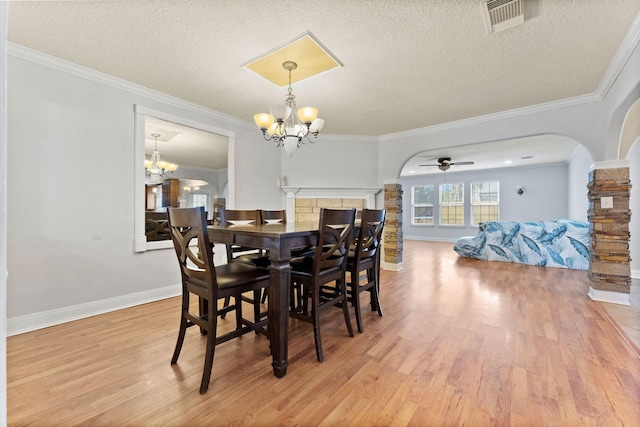 dining space with ceiling fan with notable chandelier, a textured ceiling, crown molding, a fireplace, and light hardwood / wood-style flooring