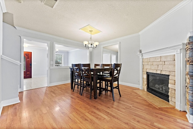 dining space with a stone fireplace, hardwood / wood-style floors, ornamental molding, and a textured ceiling