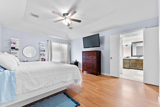 bedroom featuring a textured ceiling, ensuite bath, wood-type flooring, and ceiling fan