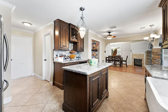 kitchen with ornamental molding, ceiling fan with notable chandelier, light tile patterned floors, a center island, and pendant lighting