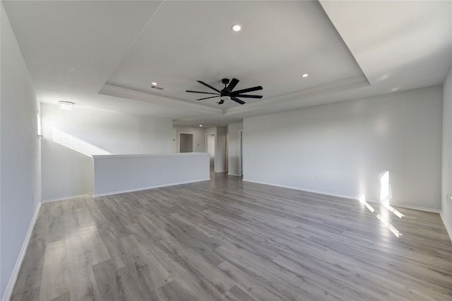 unfurnished living room with light hardwood / wood-style flooring, ceiling fan, and a raised ceiling