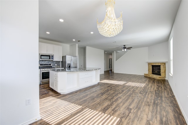 kitchen with a stone fireplace, stainless steel appliances, a center island with sink, white cabinetry, and ceiling fan with notable chandelier