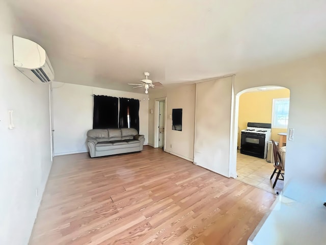 living room with a wall unit AC, light hardwood / wood-style flooring, and ceiling fan