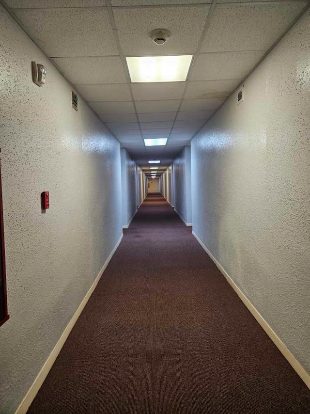 hall with dark colored carpet and a paneled ceiling