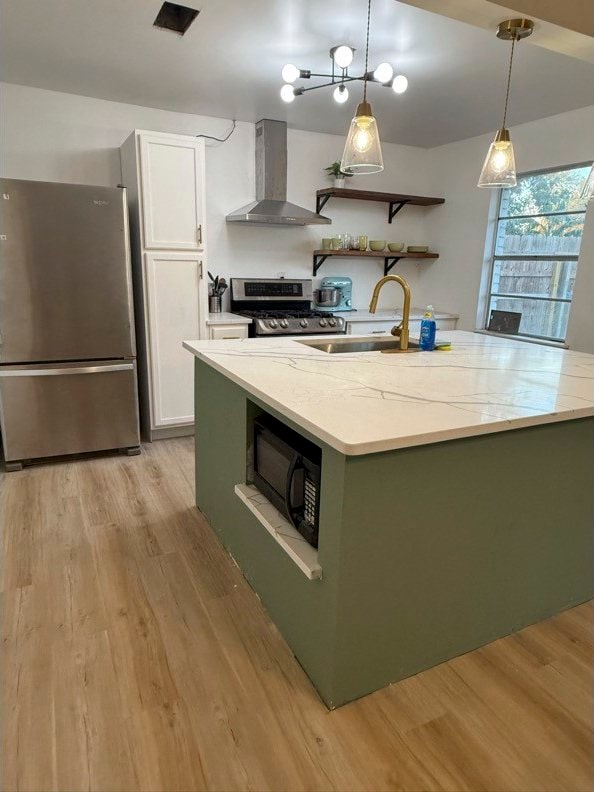 kitchen with stainless steel appliances, light wood-style floors, wall chimney exhaust hood, and open shelves