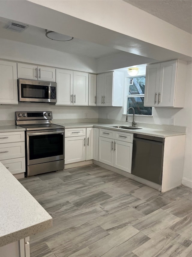 kitchen featuring appliances with stainless steel finishes, light hardwood / wood-style flooring, white cabinetry, and sink