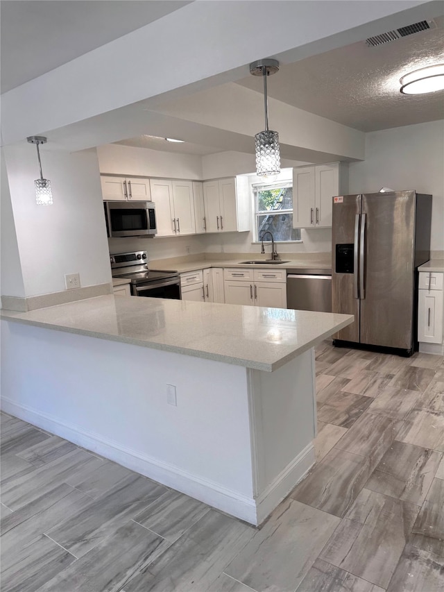 kitchen featuring hanging light fixtures, kitchen peninsula, stainless steel appliances, sink, and white cabinets