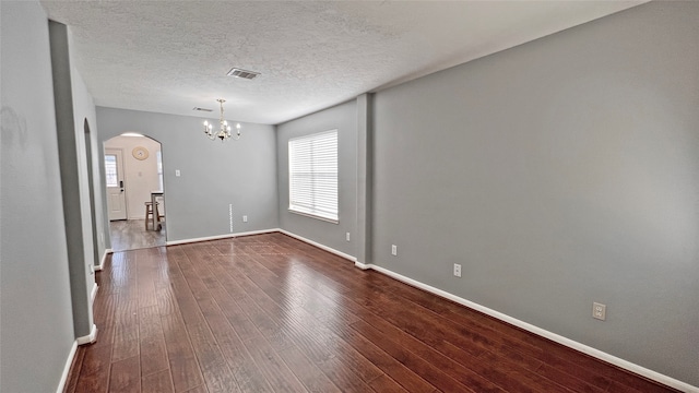 empty room featuring dark hardwood / wood-style flooring, a textured ceiling, and a notable chandelier