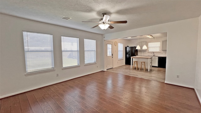 unfurnished living room with hardwood / wood-style flooring, ceiling fan, sink, and a textured ceiling