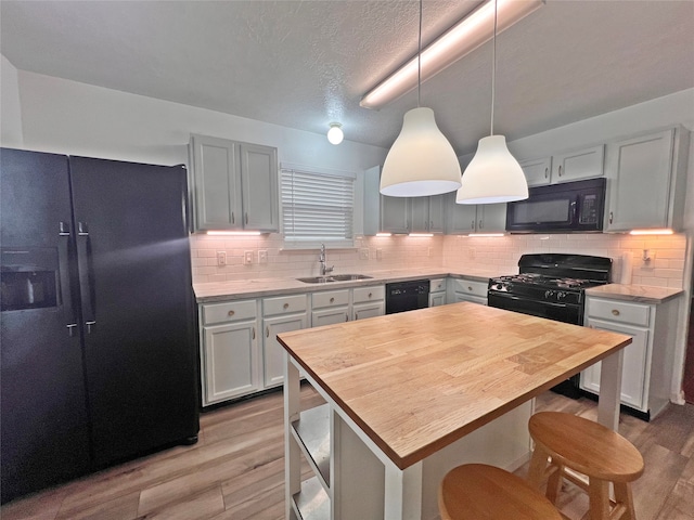 kitchen with sink, a center island, light hardwood / wood-style floors, decorative backsplash, and black appliances