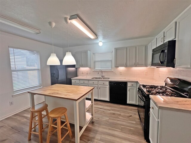 kitchen featuring a center island, black appliances, a kitchen breakfast bar, light wood-type flooring, and white cabinetry