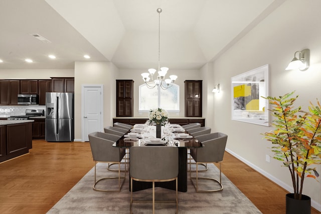 dining area with hardwood / wood-style floors, vaulted ceiling, and a notable chandelier