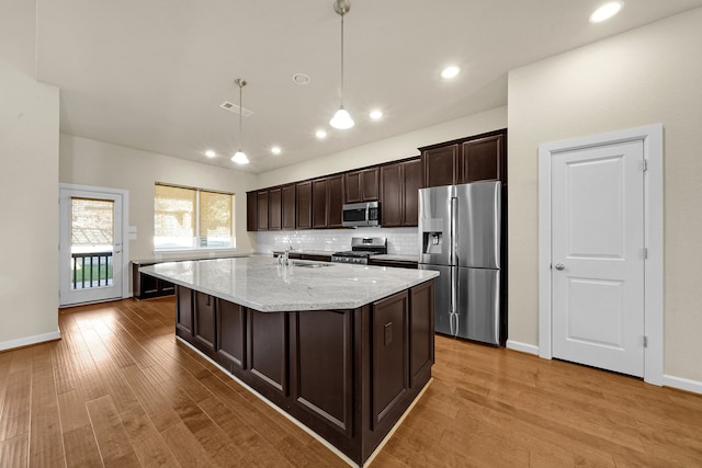 kitchen with light stone countertops, appliances with stainless steel finishes, dark brown cabinetry, pendant lighting, and light hardwood / wood-style flooring