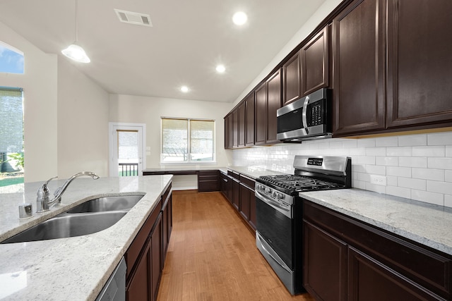 kitchen featuring appliances with stainless steel finishes, sink, decorative light fixtures, light stone counters, and light hardwood / wood-style flooring