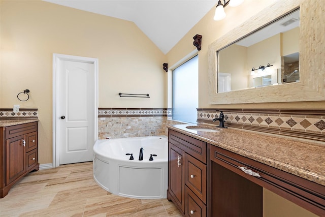 bathroom featuring tile walls, vanity, a bath, and vaulted ceiling