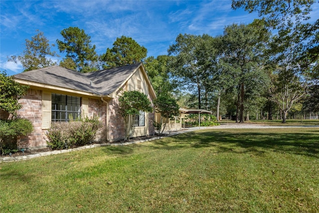 view of home's exterior featuring brick siding, a lawn, roof with shingles, and a carport