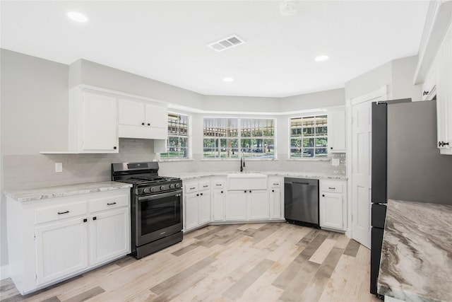 kitchen featuring backsplash, appliances with stainless steel finishes, a sink, light stone counters, and white cabinetry