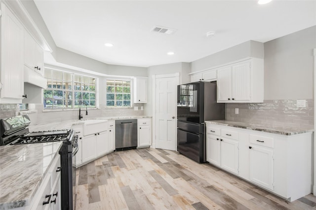 kitchen with visible vents, white cabinets, a sink, backsplash, and black appliances