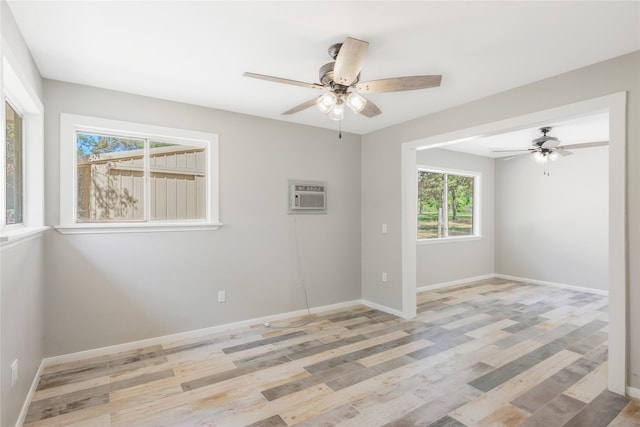 unfurnished room featuring ceiling fan, a wall mounted AC, baseboards, and light wood-type flooring