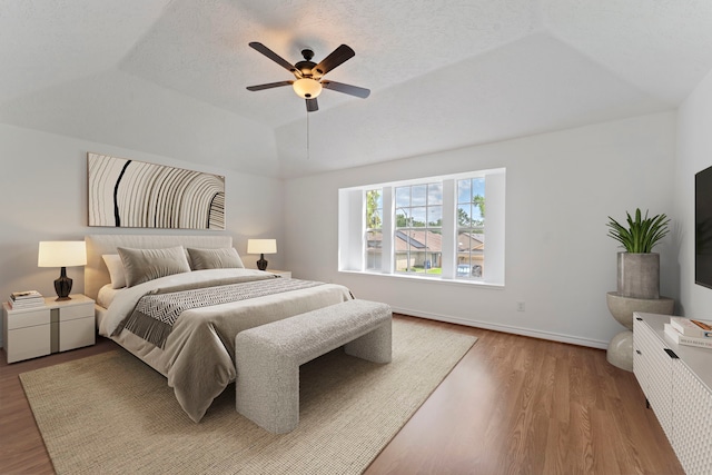 bedroom featuring vaulted ceiling, a textured ceiling, a tray ceiling, ceiling fan, and hardwood / wood-style floors