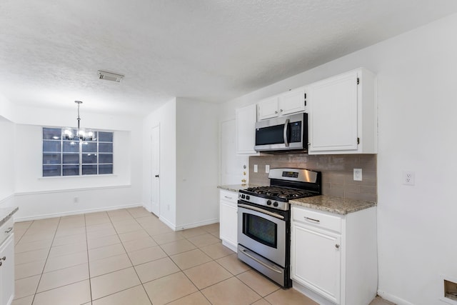 kitchen with appliances with stainless steel finishes, hanging light fixtures, light stone countertops, white cabinets, and decorative backsplash