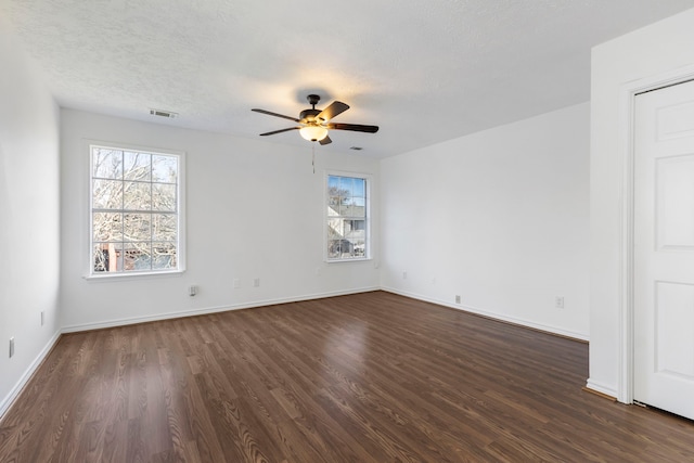 spare room with ceiling fan, a healthy amount of sunlight, a textured ceiling, and dark hardwood / wood-style flooring