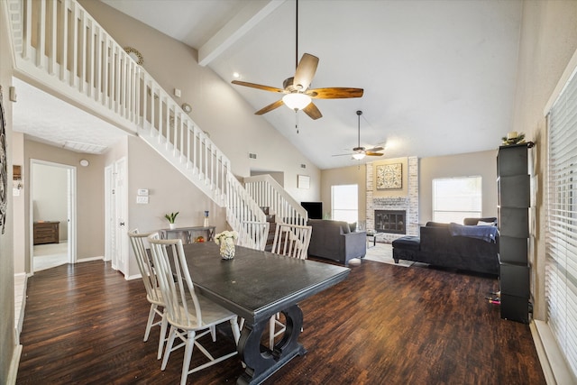 dining space featuring a stone fireplace, dark hardwood / wood-style flooring, ceiling fan, beam ceiling, and high vaulted ceiling