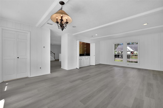 unfurnished living room featuring beam ceiling, a textured ceiling, light hardwood / wood-style flooring, and an inviting chandelier