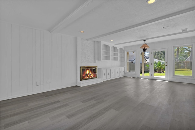 unfurnished living room with hardwood / wood-style flooring, beamed ceiling, a brick fireplace, built in features, and a textured ceiling