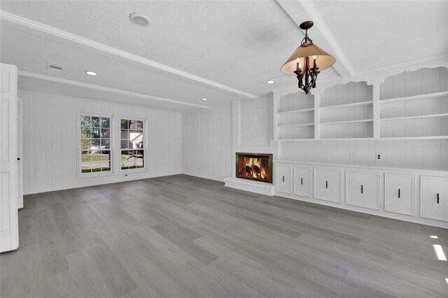 unfurnished living room featuring built in features, a brick fireplace, light hardwood / wood-style floors, wooden walls, and a notable chandelier